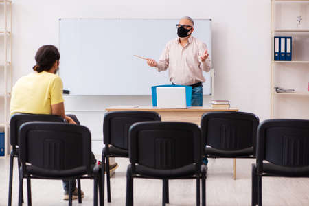 Young male student and experienced teacher in pandemic conceptの写真素材