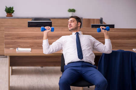 Young businessman employee doing sport exercises at workplaceの写真素材