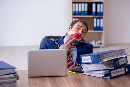 Chained male employee unhappy with excessive work in the officeの写真素材