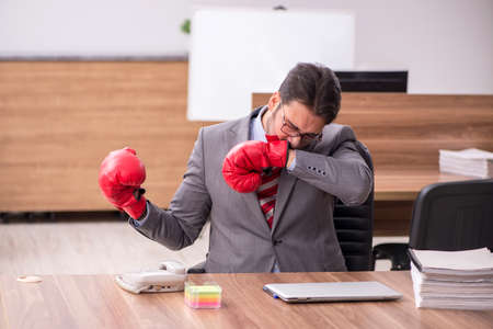 Young male employee wearing boxing gloves at workplaceの写真素材