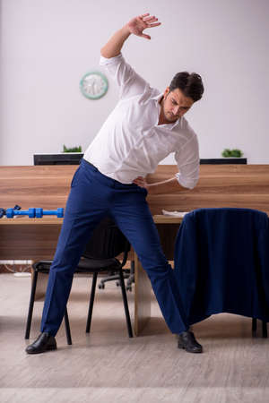 Young businessman employee doing sport exercises at workplaceの写真素材
