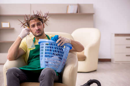 Young male contractor wearing prickly wreath on head cleaning the houseの写真素材