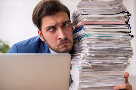 Young male employee and too much work in the officeの写真素材