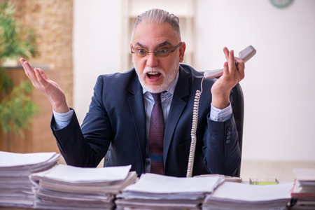 Old businessman employee unhappy with excessive work in the officeの写真素材