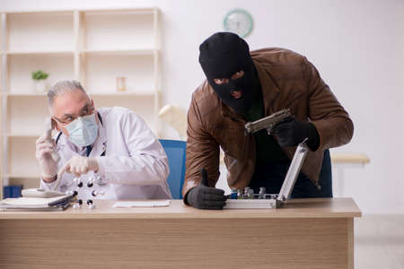 Masked man burglar stealing vaccine from old doctorの写真素材