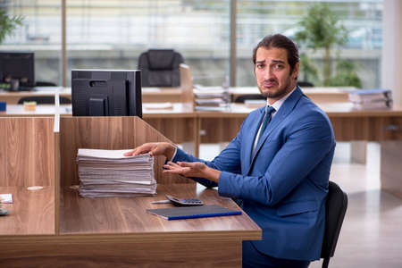 Young male employee unhappy with excessive work in the officeの写真素材