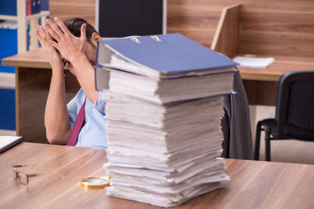 Young male employee unhappy with excessive work in the officeの写真素材