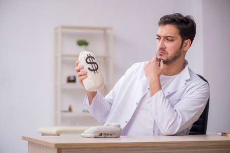 Young male doctor holding moneybag in remuneration conceptの写真素材