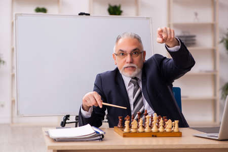 Old male employee playing chess at workplaceの写真素材