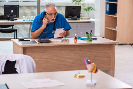 Old male doctor working in the clinic in telemedicine conceptの写真素材