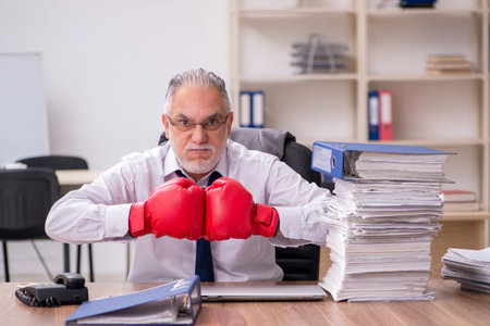Old businessman employee wearing boxing gloves at workplaceの写真素材