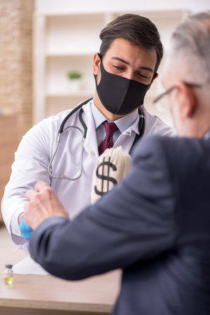 Old businessman visiting young male doctor in vaccination concepの写真素材