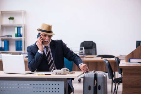 Old male employee preparing for travel in the officeの写真素材