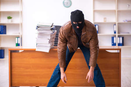Young man in balaclava stealing information from the officeの写真素材