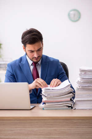 Young male employee and too much work in the officeの写真素材