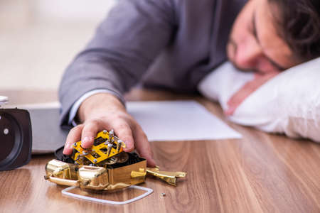 Young male employee in oversleeping conceptの写真素材