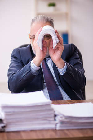 Old businessman employee unhappy with excessive work in the officeの写真素材