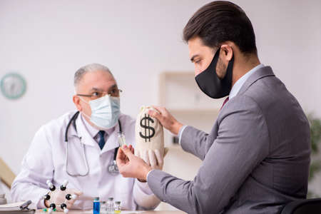 Young businessman visiting old male doctor in vaccination concepの写真素材