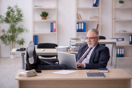 Old male employee sitting at workplaceの写真素材