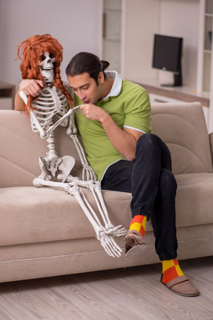Young man sitting on the sofa with female skeletonの写真素材