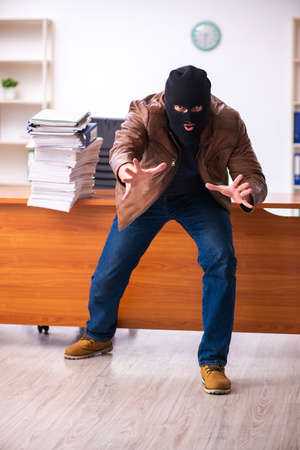 Young man in balaclava stealing information from the officeの写真素材