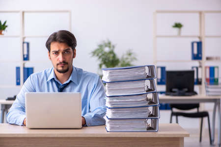 Young male employee and too much work in the officeの写真素材