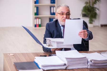 Old businessman employee unhappy with excessive work in the officeの写真素材