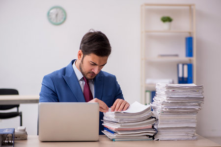 Young male employee and too much work in the officeの写真素材