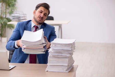 Young male employee and too much work in the officeの写真素材