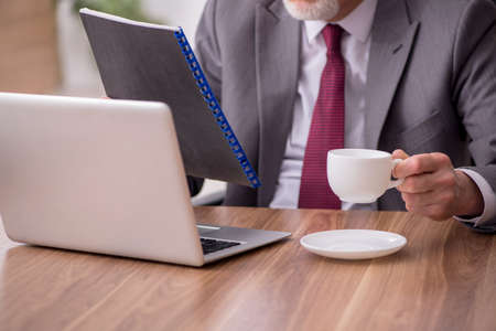Old male employee drinking tea during breakの写真素材