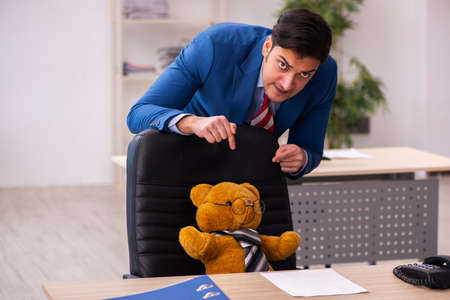 Young male employee and his toy bear boss in funny conceptの写真素材