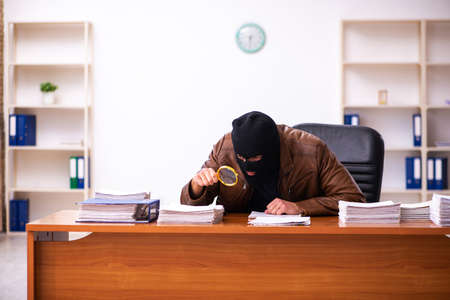 Young man in balaclava stealing information from the officeの写真素材