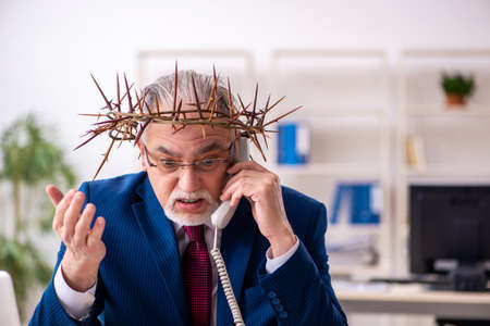 Old male employee wearing prickly wreath on headの写真素材