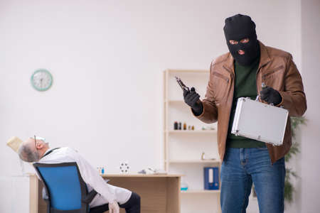 Masked man burglar stealing vaccine from old doctor