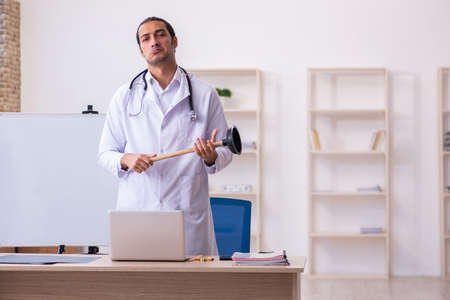 Young male doctor holding plunger in funny conceptの写真素材