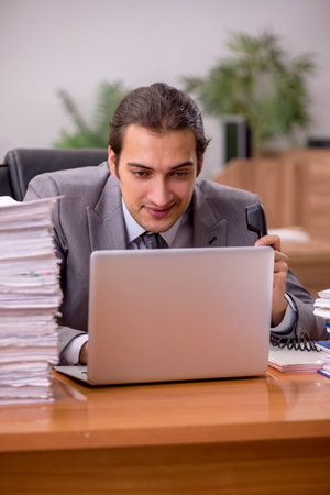 Young male employee and too much work in the officeの写真素材