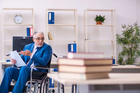 Old male employee in wheel-chair sitting in the officeの写真素材