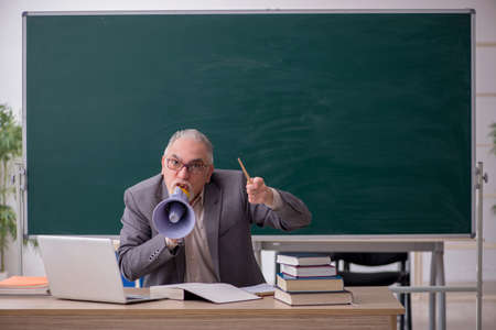Old male teacher holding megaphone in front of blackboardの写真素材