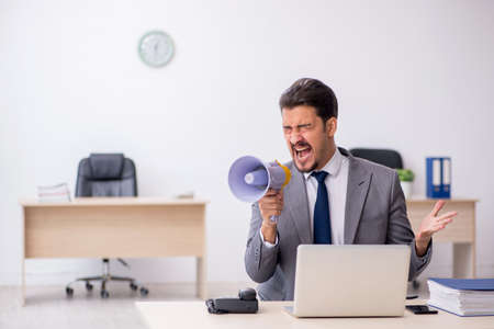 Young male employee holding megaphone at workplaceの写真素材