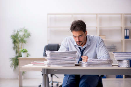 Young male employee unhappy with excessive work in the officeの写真素材