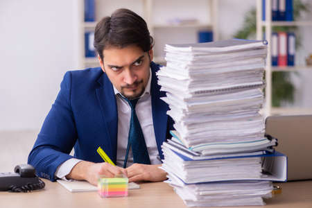Young male employee and too much work in the officeの写真素材