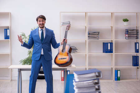 Young male employee playing guitar at workplaceの写真素材