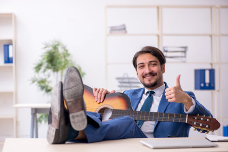 Young male employee playing guitar at workplaceの写真素材
