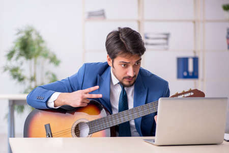 Young male employee playing guitar at workplaceの写真素材