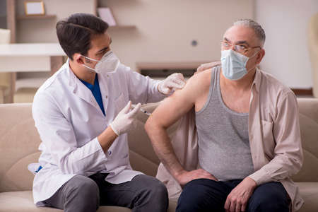 Young male doctor visiting old patient in vaccination conceptの写真素材