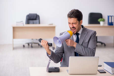 Young male employee holding megaphone at workplaceの写真素材