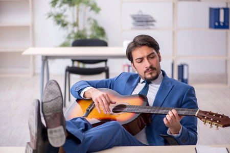 Young male employee playing guitar at workplaceの写真素材