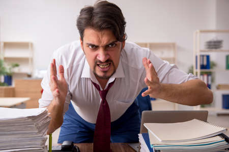 Young male employee and too much work in the officeの写真素材