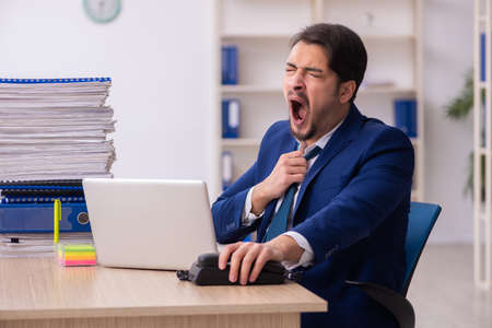 Young male employee and too much work in the officeの写真素材