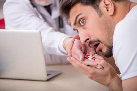 Old male doctor suggesting pills to young male patientの写真素材